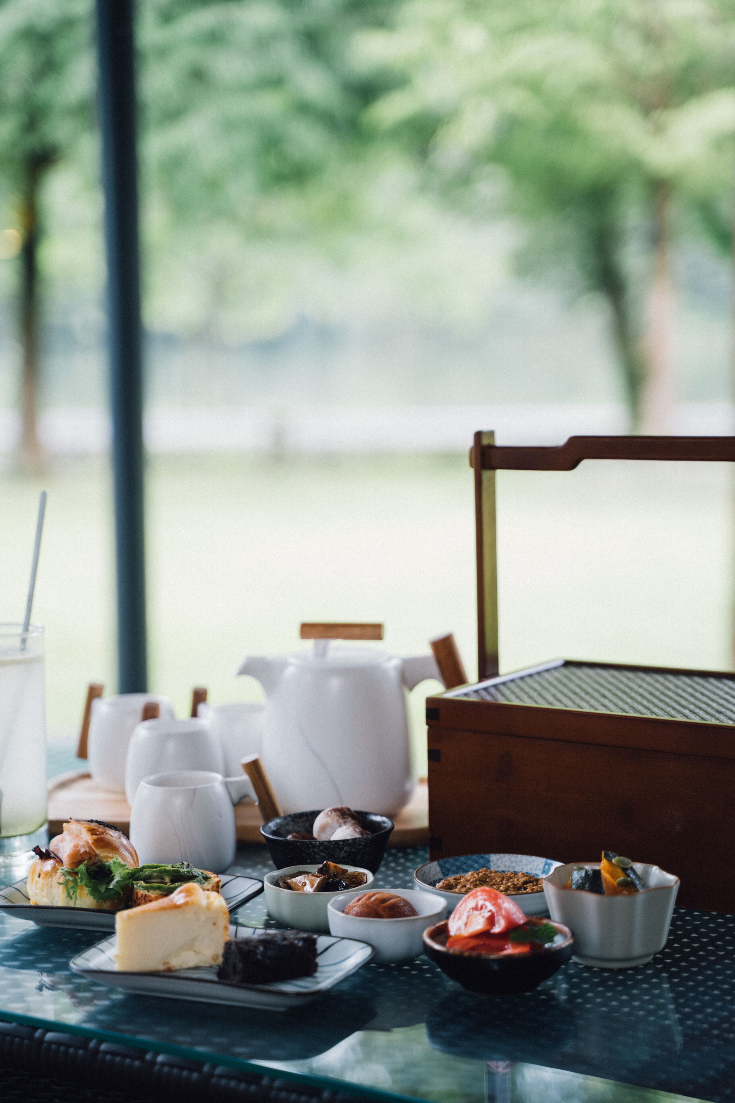 Una mesa con diversos platos y una tetera, ubicada en una habitación con vistas a zonas verdes.
