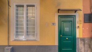 A green door with a window above it, a utility box, and a yellow wall.
