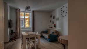 A cozy living room with a wooden dining table, a sofa, and a TV mounted on the wall.