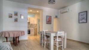 A dining area with a table and chairs, a kitchen in the background, and artwork on the walls.