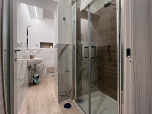 Features a sleek shower, white sink, and minimalist design.