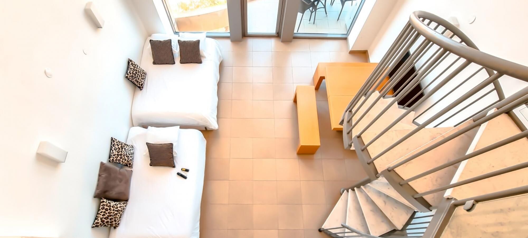 Ein modernes Hotelzimmer mit einer Sitzecke, einer hölzernen Bank und einer Treppe mit Metallgeländern.