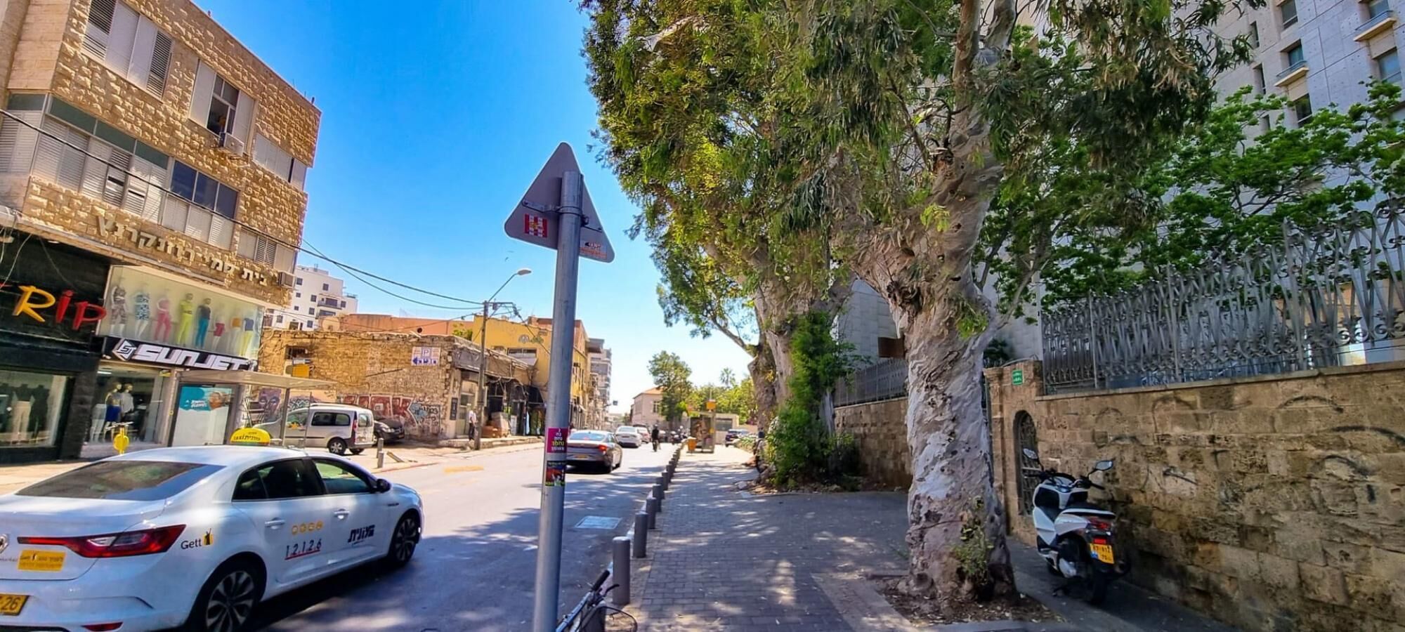 A street scene with a white car parked on the side, a tree, and a building with a sign that reads "Sunjet".