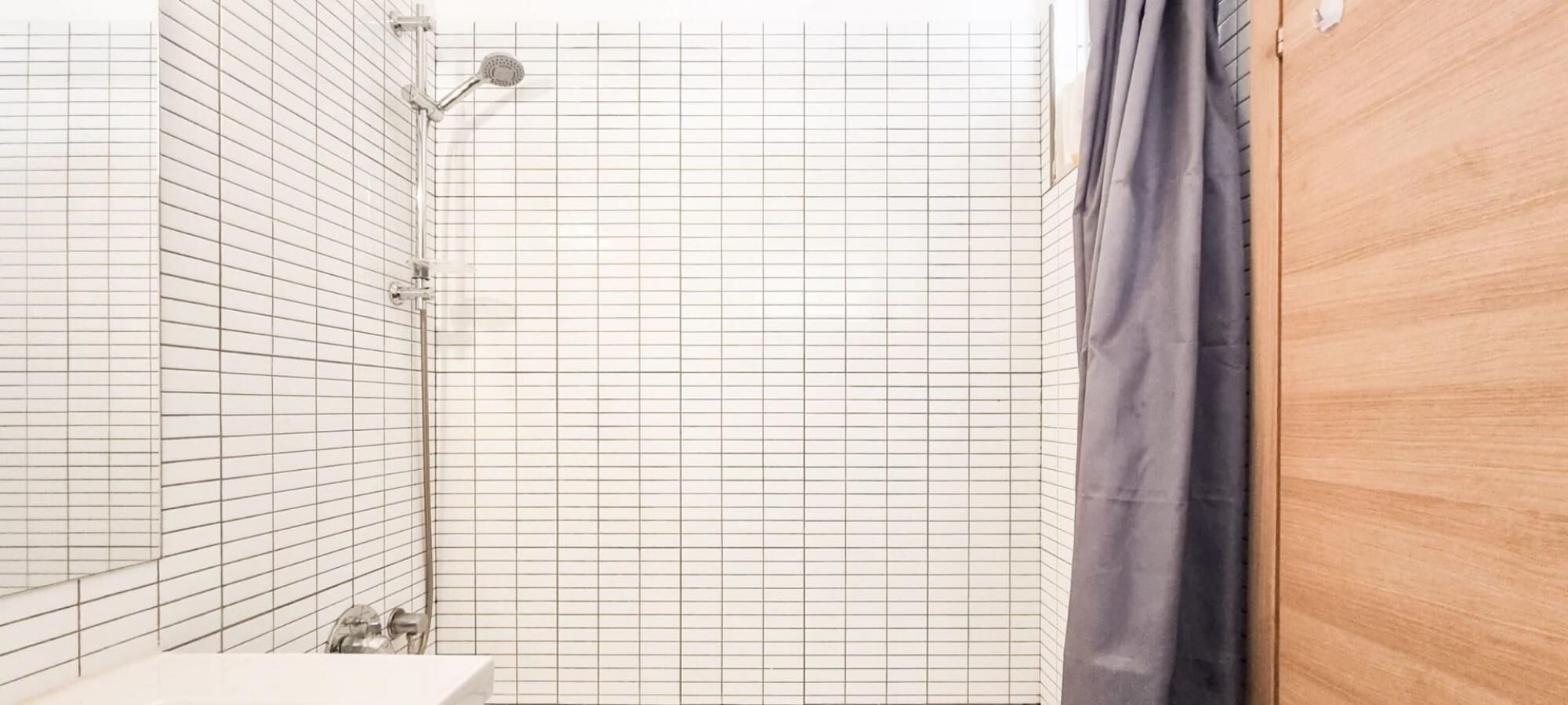 A bathroom with a grid-patterned wall, a shower, and a wooden door.