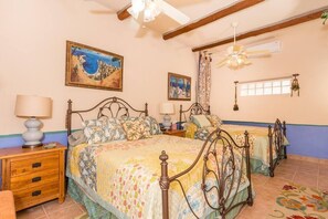 A bedroom with two beds, a ceiling fan, and artwork on the walls.