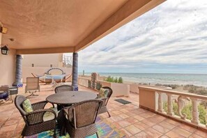 An outdoor patio with a round table and chairs, a view of the ocean, and a balcony railing.