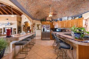 A kitchen with a brick ceiling, wooden cabinets, a central island with bar stools, and a refrigerator.