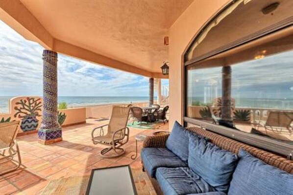 A balcony with a view of the sea, a sofa, and a chair.
