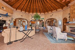 A spacious living area with a high wooden ceiling, a central seating area with a sofa and armchairs, a coffee table, and a fireplace.