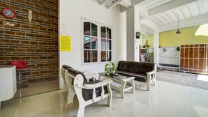 A room with a brick wall, a white sofa, a coffee table, and a red chair. - Hotel O Guesthouse King Puntodewo (Banguntapan)