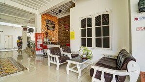 A spacious lobby with white furniture, a large window, and a brick wall with a sign. - Hotel O Guesthouse King Puntodewo (Banguntapan)