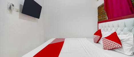 A neatly made bed with white and red bedding, a mounted television, and a red curtain.
