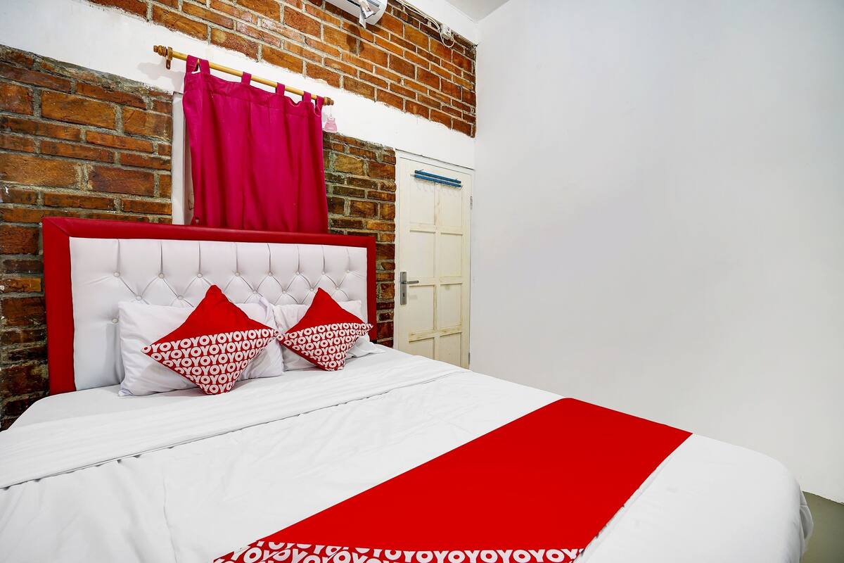 Ein Schlafzimmer mit Backsteinwand, einem weißen Bett mit roten Akzenten und einer Tür mit blauer Klinke.