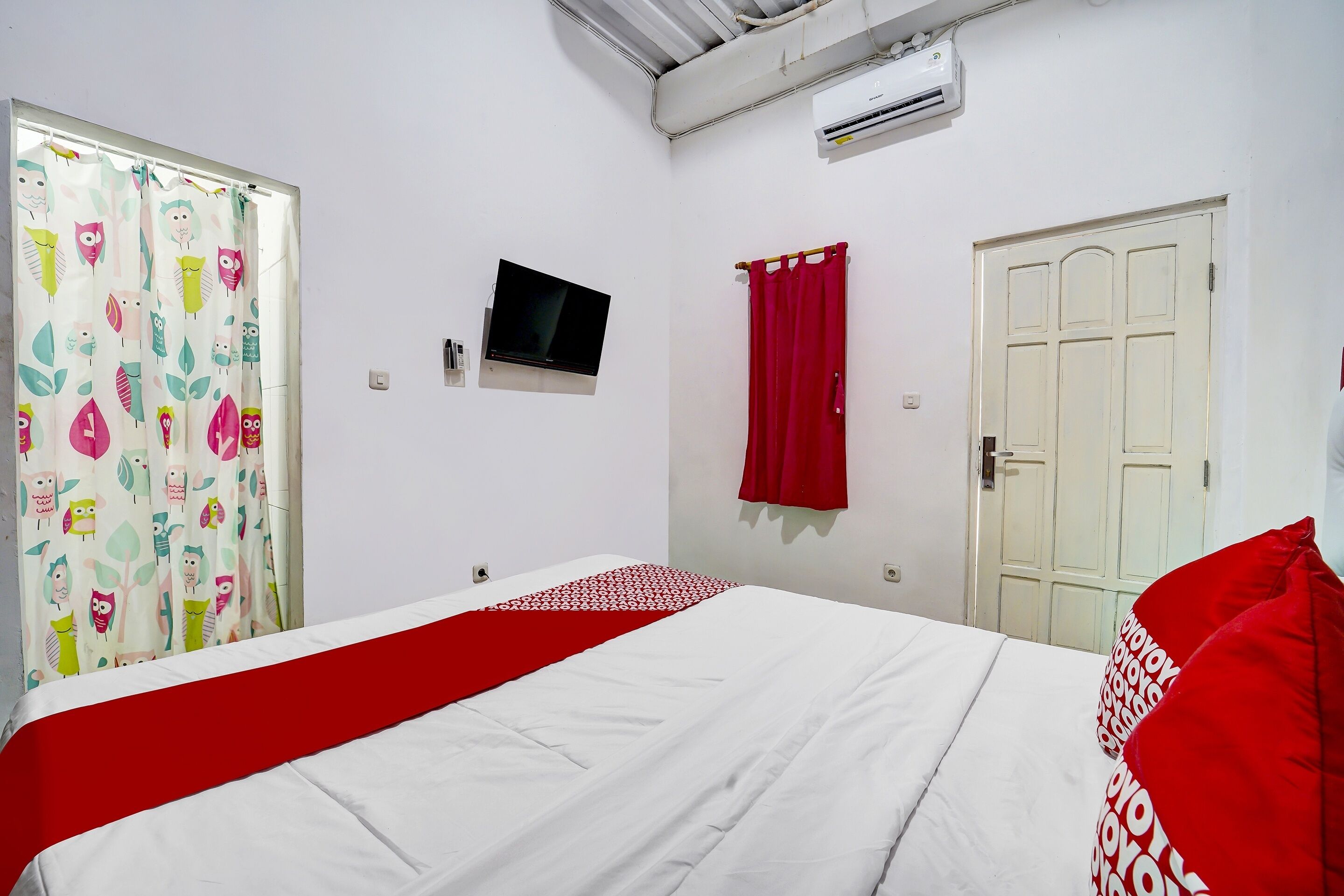 A bedroom with a bed, a TV, a wardrobe, and a window with curtains.