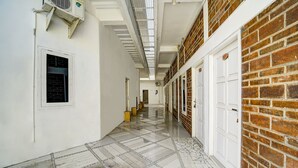 A corridor with a tiled floor, white walls, and a brick wall on one side. - Hotel O Guesthouse King Puntodewo (Banguntapan)