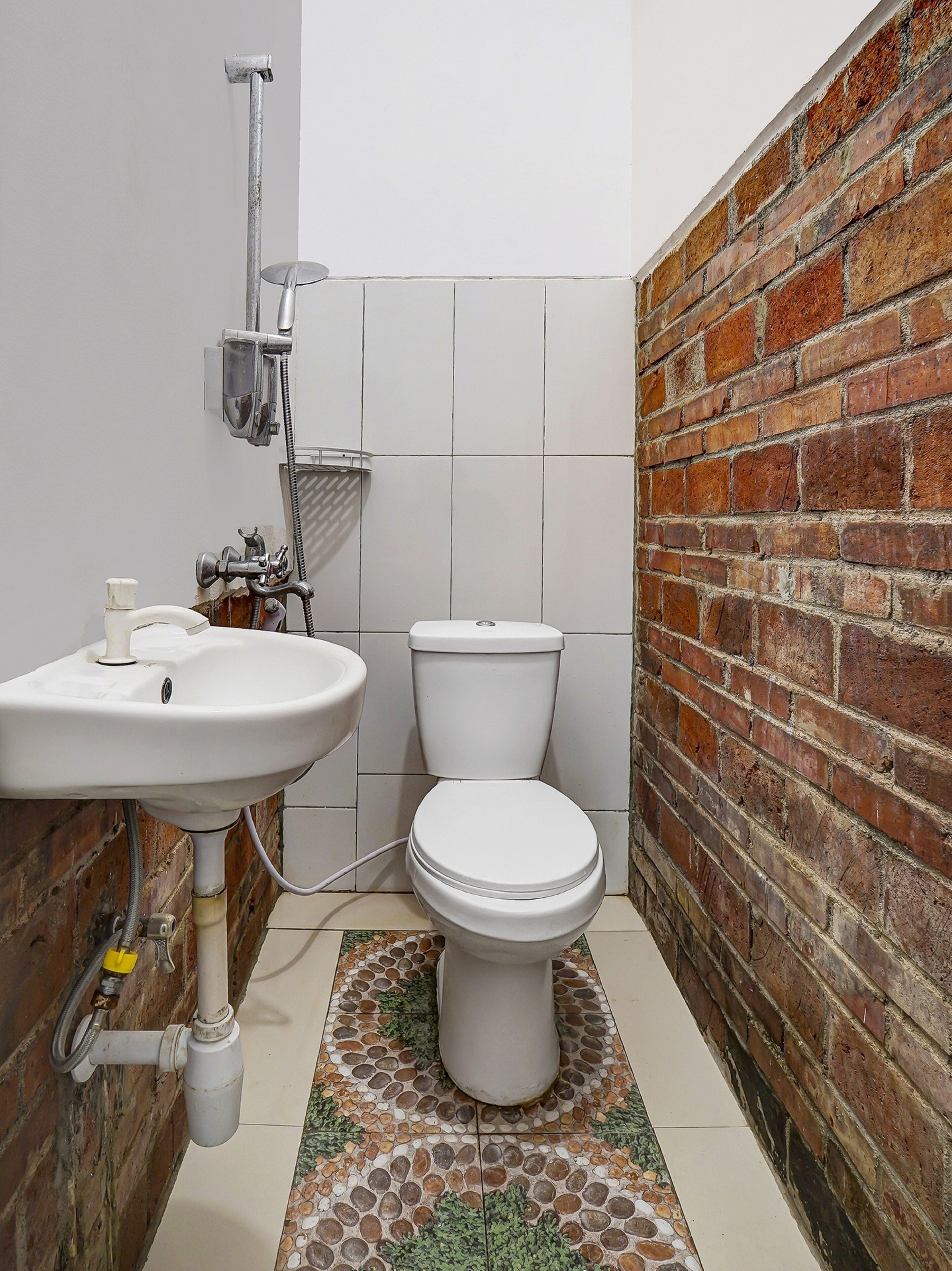 A small bathroom with a white sink, toilet, and shower. The walls are tiled, and there's a brick wall on one side.