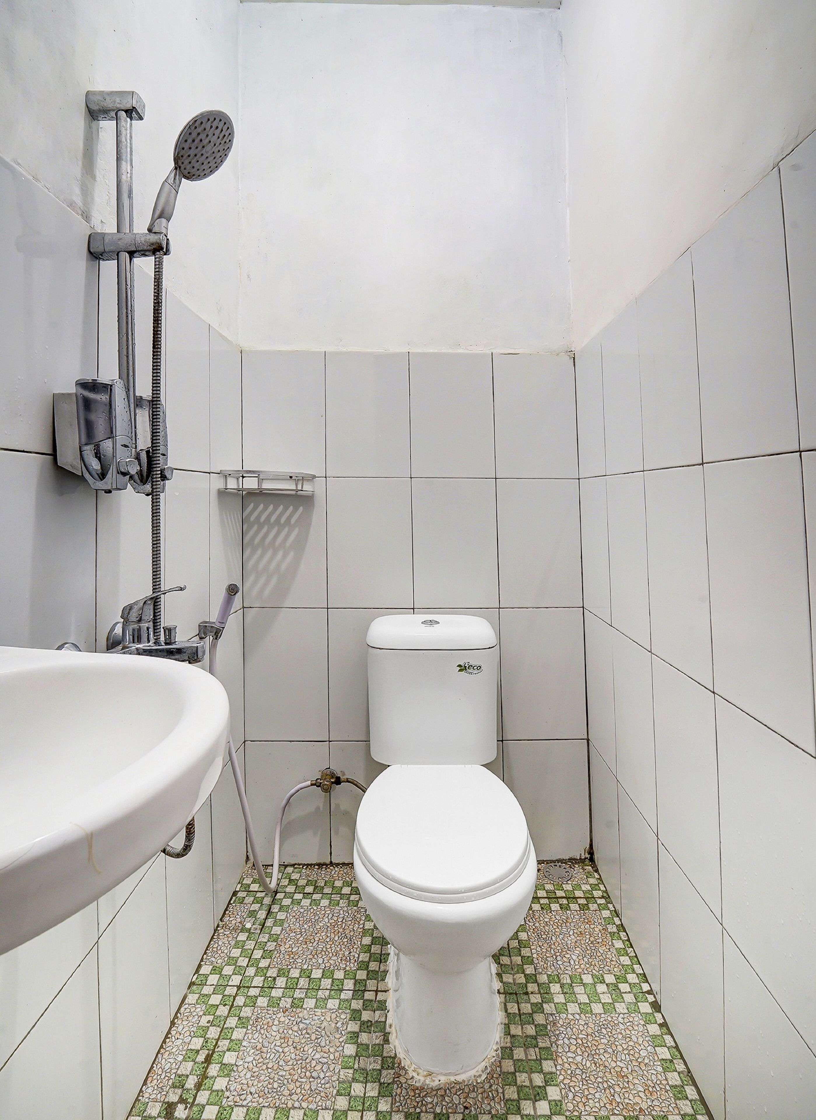 Un baño con lavamanos, inodoro y ducha blancos. El piso tiene un diseño de mosaico blanco y verde.
