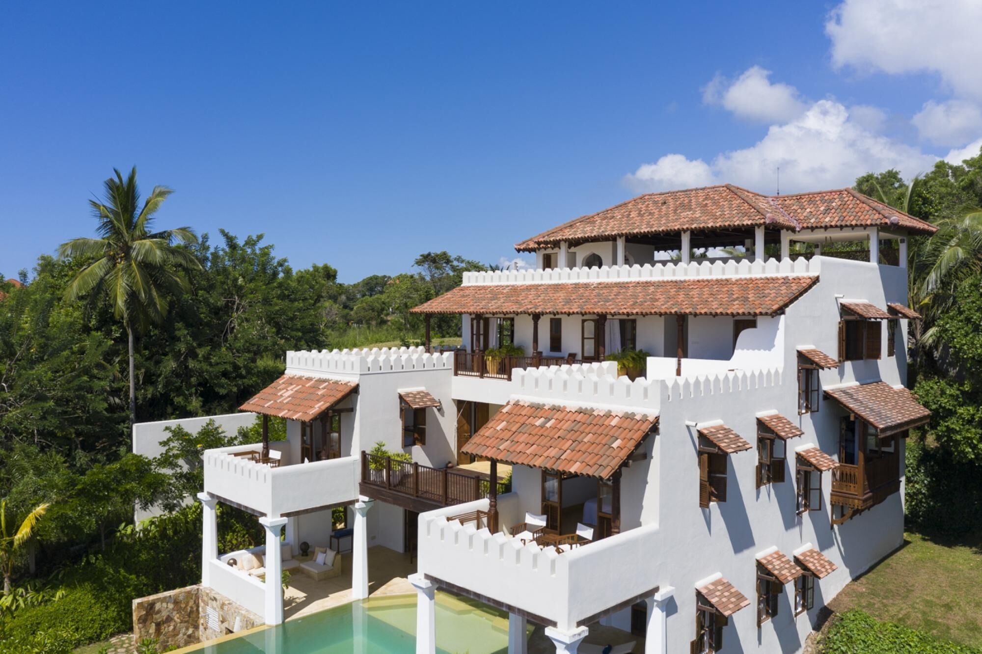 Un immeuble à plusieurs étages, à la façade blanche et au toit recouvert de tuiles en terre cuite, doté de balcons et d’une piscine.