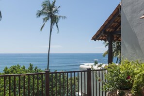 A balcony with a view of the ocean, a palm tree, and a building with a tiled roof. - Ceylon House in Weligama (Weligama)