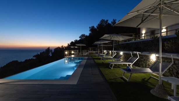 A poolside area with lounge chairs and umbrellas, overlooking a body of water. - Villa Olivella by Elite Villas (Anacapri)