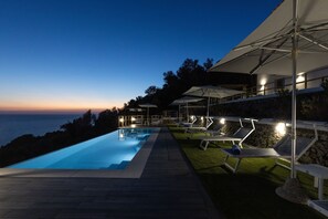 Zona piscina con sedie a sdraio e ombrelloni, con vista su un corpo d'acqua.