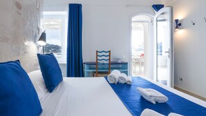A hotel room with a bed, blue bedding, a table with towels, and a view through a door. - Villa Olivella by Elite Villas (Anacapri)
