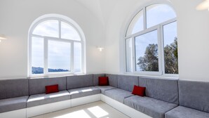 A modern living room with a grey sectional sofa, red cushions, and large arched windows offering a view of the outdoors. - Villa Olivella by Elite Villas (Anacapri)