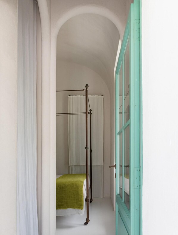 A narrow hallway with a four-poster bed, a green bedspread, and a teal door. - Capri Designer Suite by Elite Villas (Capri)