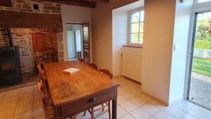 Un espace repas avec une table et des chaises en bois, un mur en pierre, un plafond en bois et une fenêtre donnant sur un paysage verdoyant.