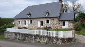 Une maison en pierre avec un toit gris, des volets blancs et une clôture en bois peinte en blanc.