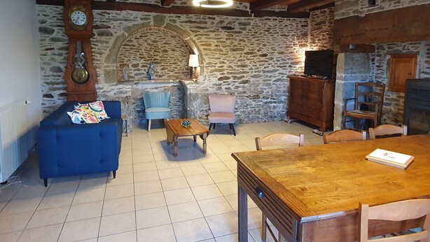 Un salon rustique avec des murs en pierre, un plafond en bois, un canapé bleu, une table en bois et un téléviseur.