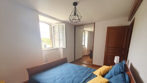 Une chambre à coucher avec un lit, une tête de lit en bois, une fenêtre, un miroir et une porte.
