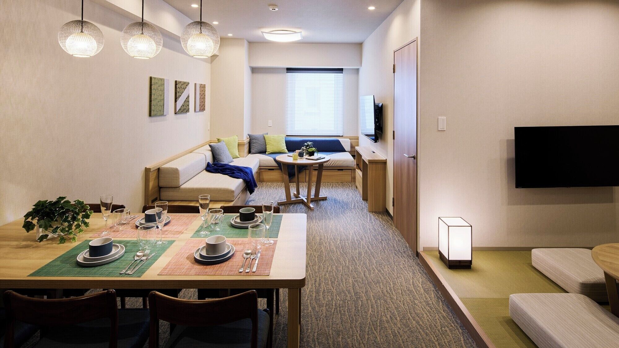 A modern living room with a sofa, a dining table set with plates and glasses, and a TV mounted on the wall.