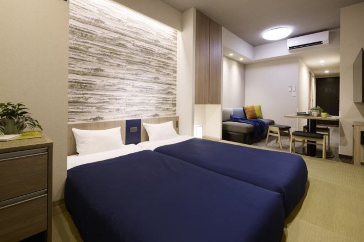 A hotel room with a large bed, a desk, a chair, and a small table.