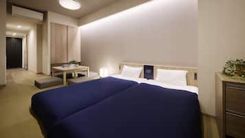 A hotel room with a large bed, a bedside table with a lamp, a small desk, and a potted plant.
