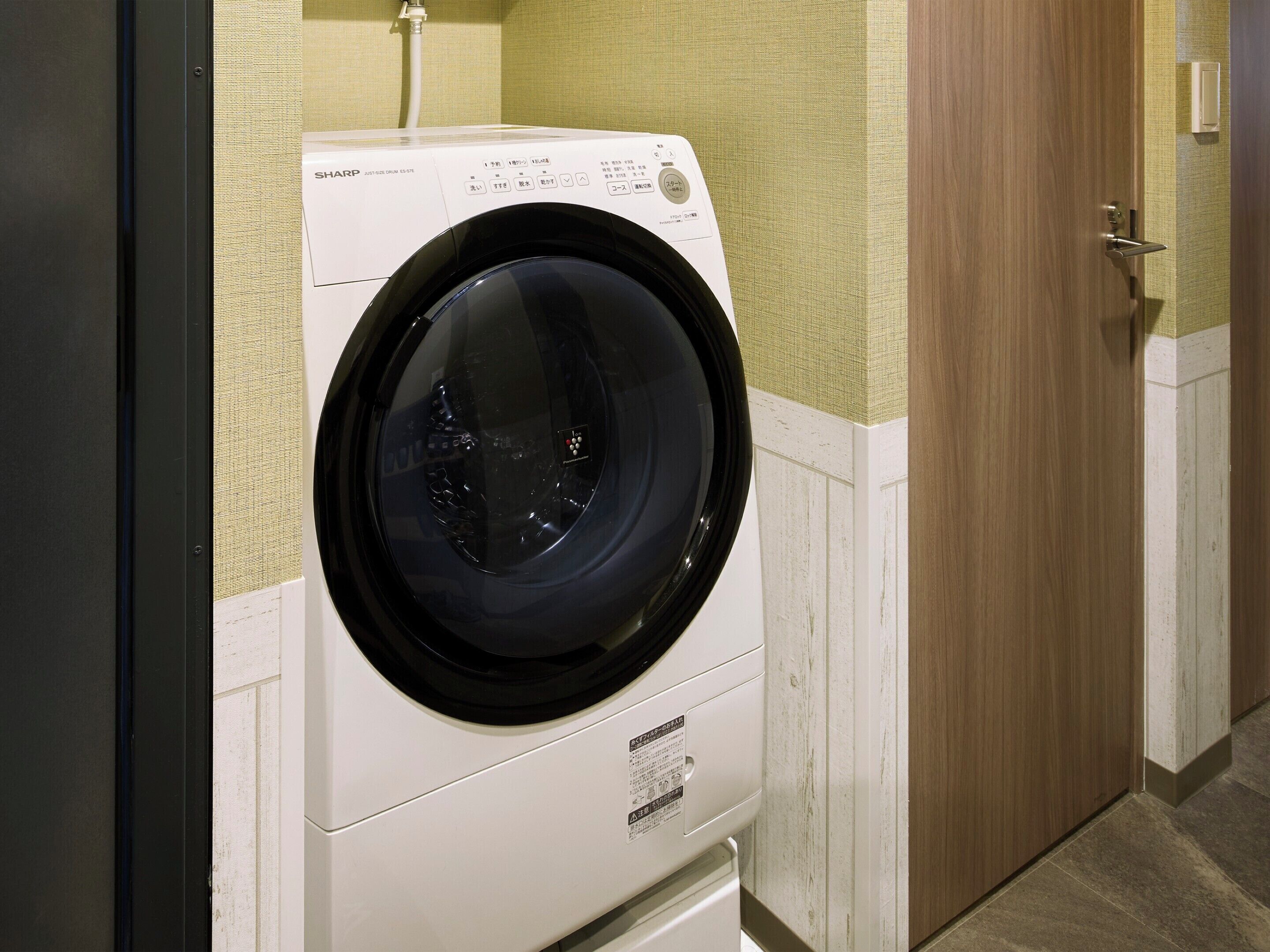 A front-loading washing machine in a room with wooden doors and a textured wall.