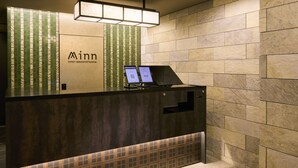 A hotel reception desk with a digital screen and a QR code, a tiled wall with the hotel's name, and a modern light fixture above. - Minn Ueno Shin-Okachimachi (Tokyo)