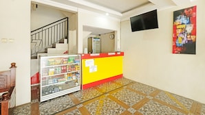 Un vestíbulo de hotel con una recepción, una máquina expendedora, una escalera y un televisor instalado en la pared.