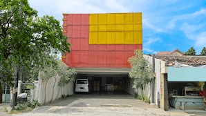 Un edificio con una fachada grande, roja y amarilla, un acceso cubierto y una furgoneta estacionada en la parte delantera.