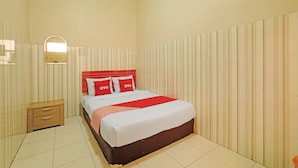 Una habitación de hotel ordenada con cama, mesita de noche y un espejo en la pared.