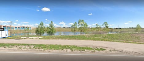 A road with a building in the background, a body of water, and sparse vegetation.