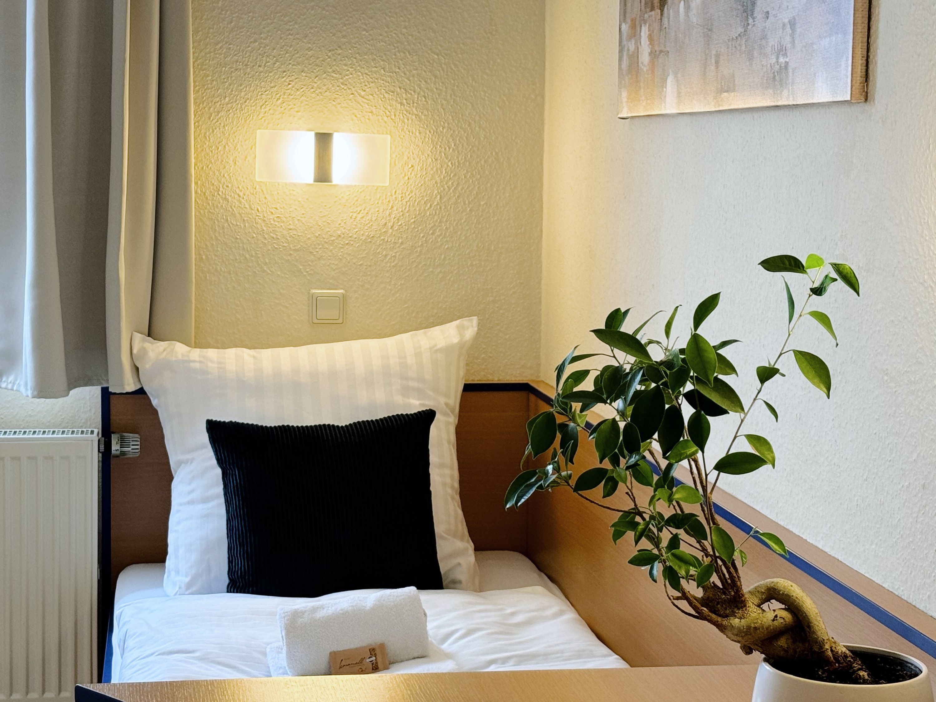 Ein Hotelzimmer mit Bett, Nachttisch, Topfpflanze und Wandleuchte.