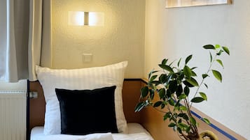 Ein Hotelzimmer mit Bett, Nachttisch, Topfpflanze und Wandleuchte.