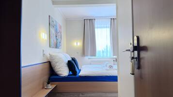 A hotel room with a bed, a small bedside table, a wall-mounted painting, and a window with curtains.