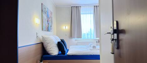 Habitación de hotel con cama, mesita de noche, un cuadro en la pared y una ventana con cortinas.
