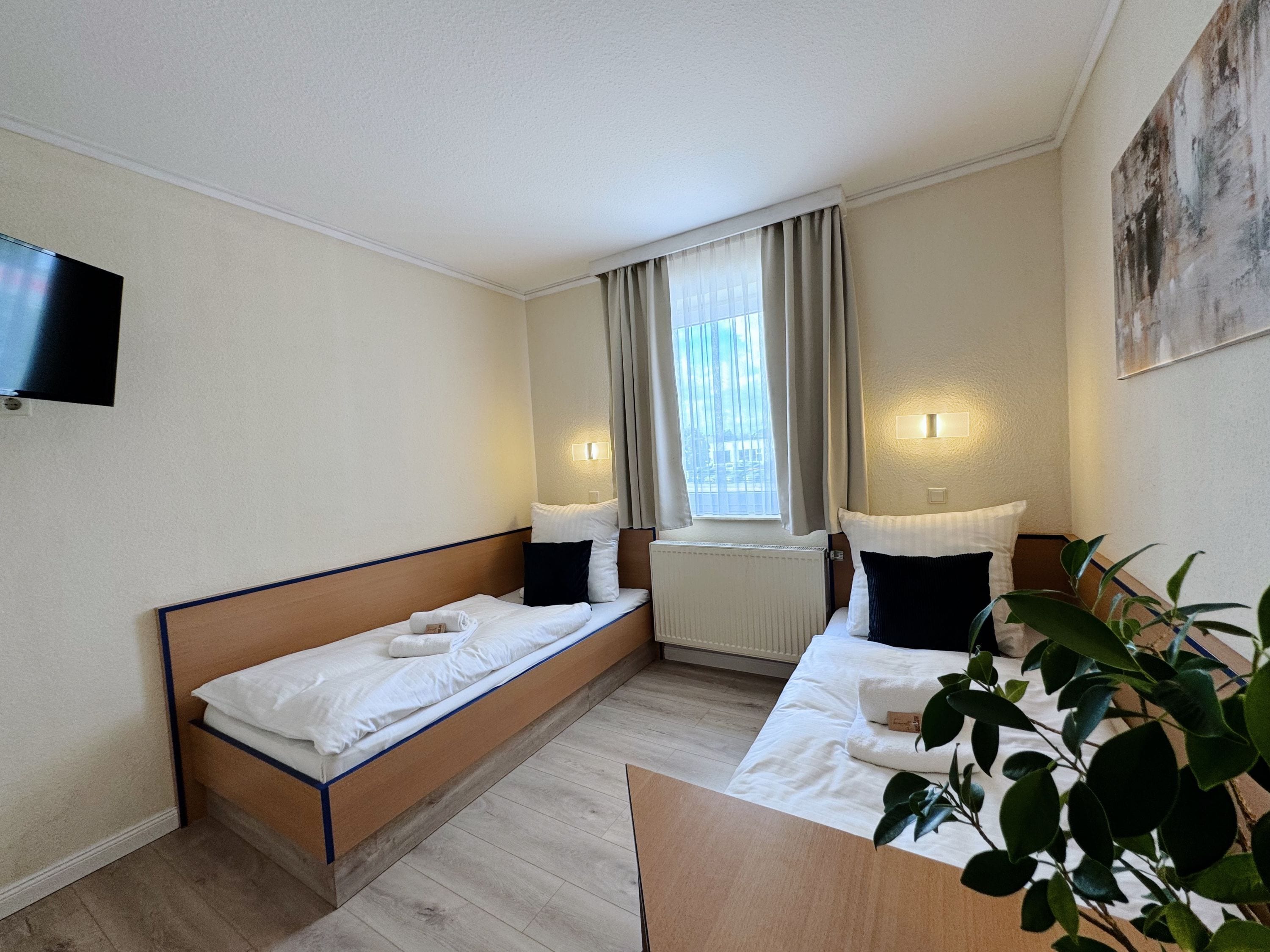Una habitación de hotel moderna con dos camas individuales, un televisor de pantalla plana, un ventanal con cortinas y un cuadro en la pared.