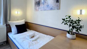 Una habitación de hotel con una cama, una mesita de noche con una planta en maceta, un cuadro en la pared y dos luces fijadas a la pared.
