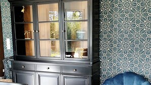 A dining area with a wooden table, chairs, a blue armchair, and a black cabinet with glass doors.