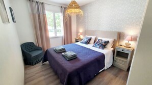 A neatly arranged bedroom with a bed, two bedside tables with lamps, a chair, and a window with curtains.