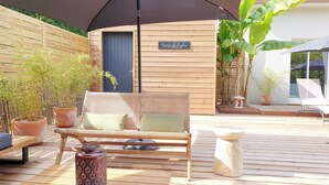 A wooden deck with a wicker sofa, a metal table, and a decorative water bottle.